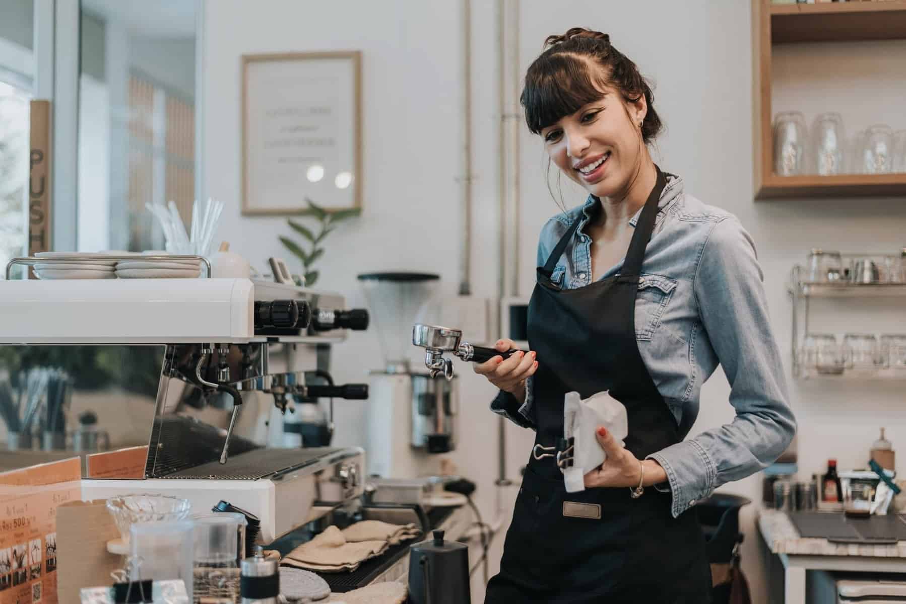 Glad kvinde kaffeejer stående bag disken på en kaffebar.