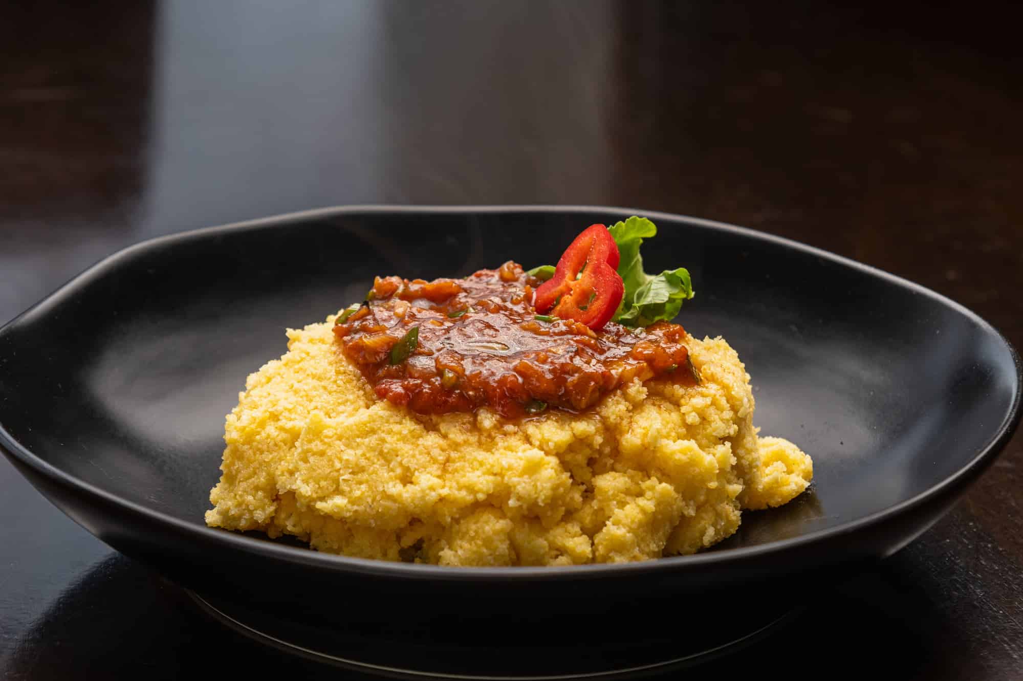 black plate of polenta with tomato sauce and melted cheese flour