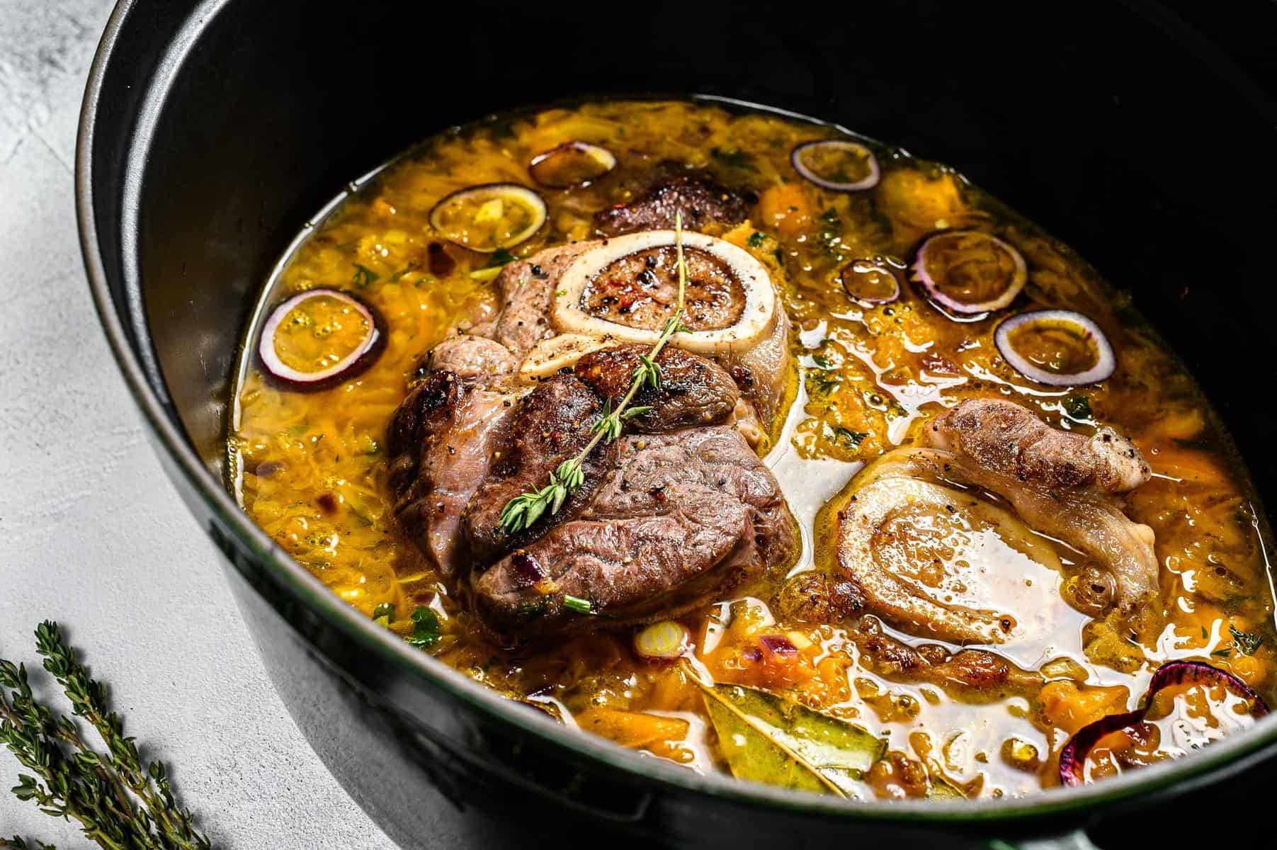 Cast iron pan with ossobuco made of cross cut veal shank. ossobuco meat stew. Gray background. Top view.