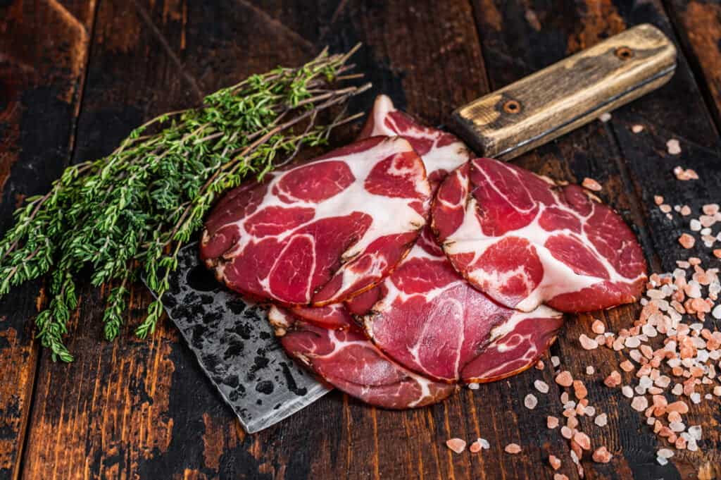 Coppa, Capocollo, Capicollo Cured ham on meat cleaver. Dark wooden background. Top view
