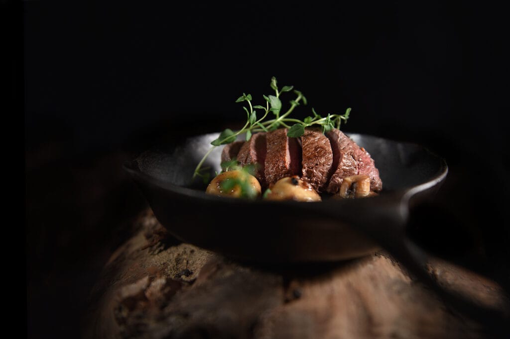 Fillet of venison, sliced and roasted with thyme herb garnish and garlic mushrooms, ready for serving