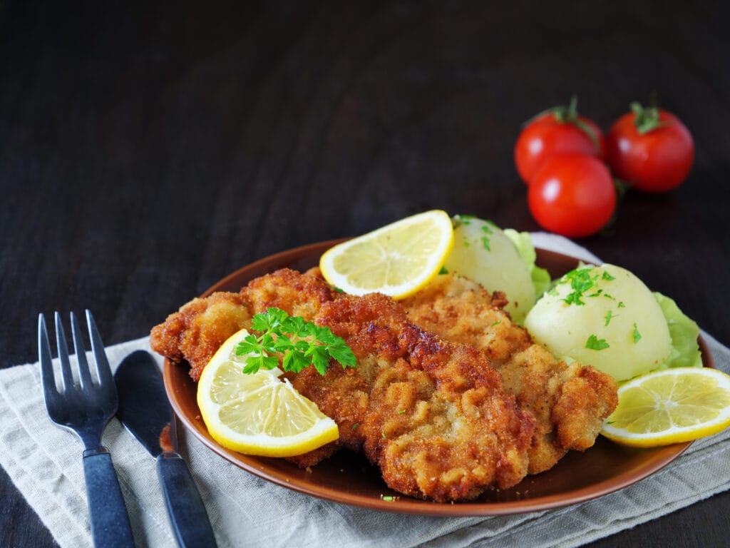 Wiener Schnitzel with potato salad served with lemon slices and parsley leaves
